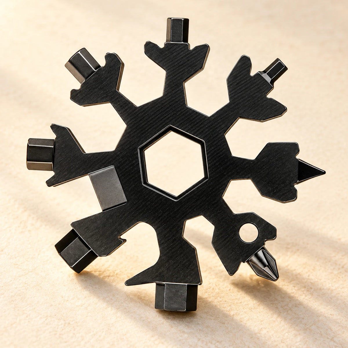 Black snowflake multi-tool on a warm neutral studio surface, showing its hexagonal center, bottle opener and driver tips